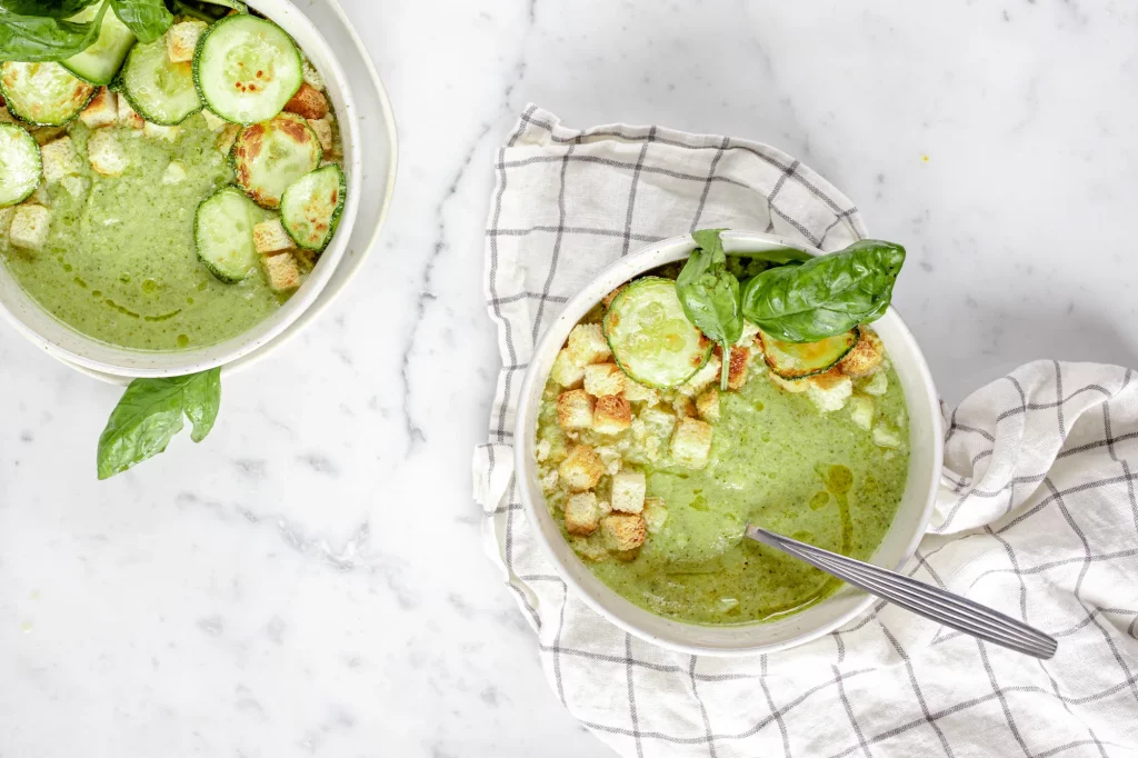 Two bowls of soup with zucchini and basil.