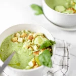 Two bowls of zucchini soup with basil and croutons.