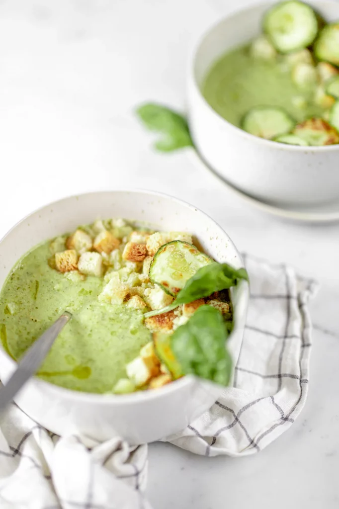 Two bowls of zucchini soup with basil and croutons.