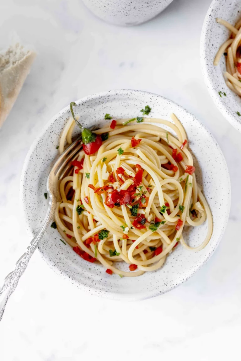 Two bowls of spaghetti with peppers and bread.