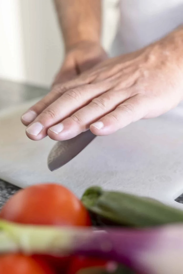 A man using a knife to cut vegetables on a cutting board.