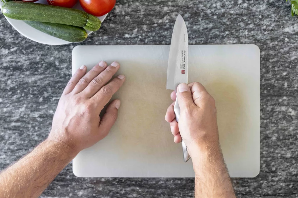 A person using a knife to cut vegetables on a cutting board.