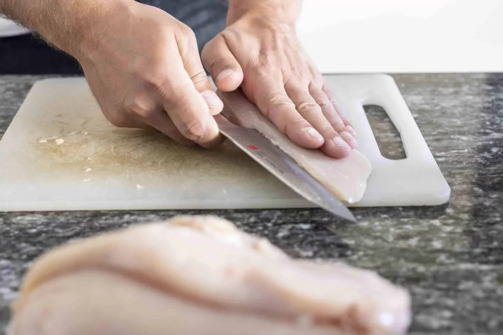 Using a knife to cut chicken on a cutting board.