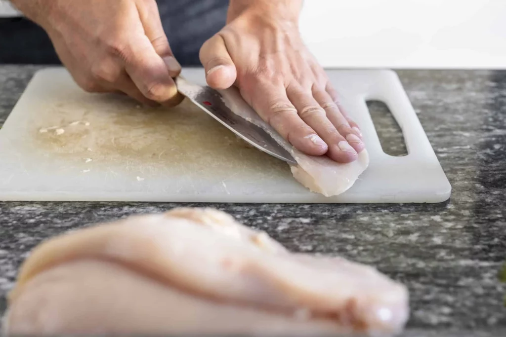 A man skillfully slicing chicken on a cutting board with a knife.