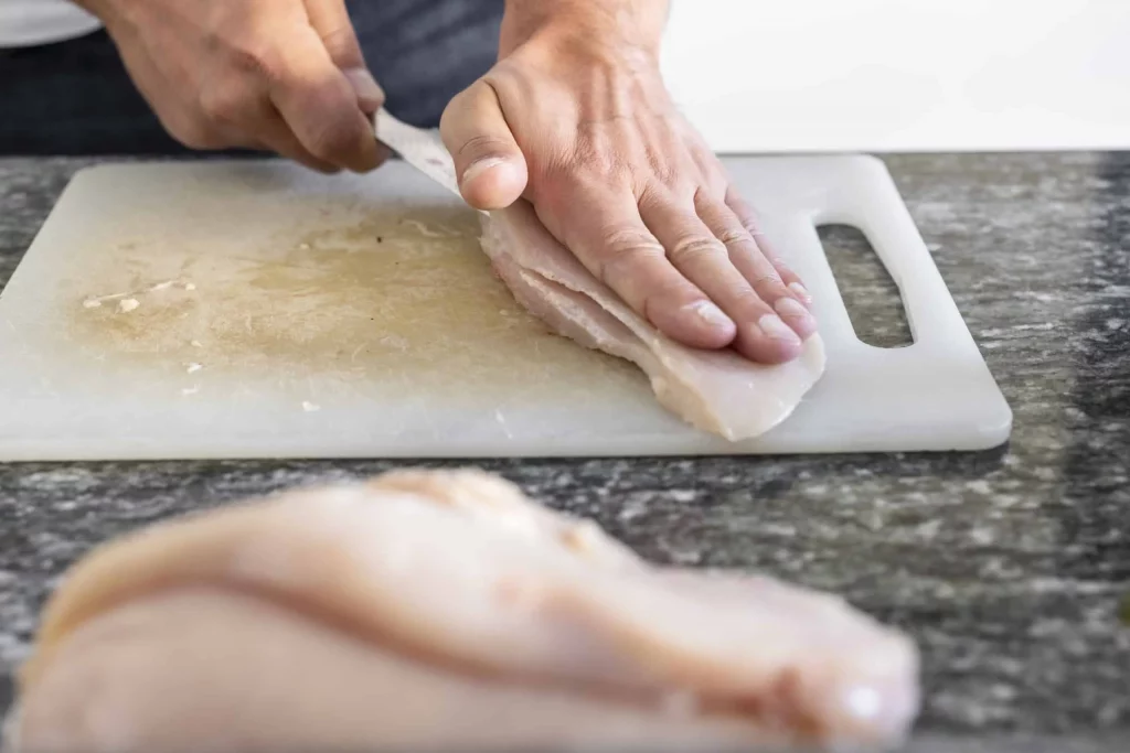 A person using a knife to slice chicken on a cutting board.