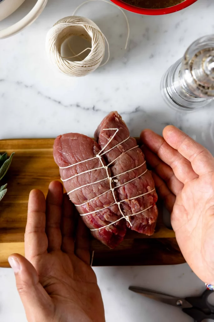 A person holding a piece of meat on a cutting board.