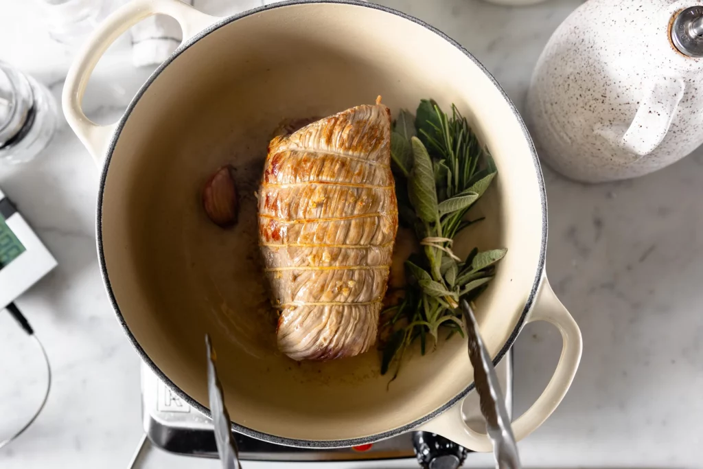 A pan with a piece of meat and sprigs of rosemary.
