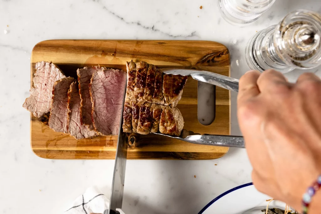 A person cutting a piece of meat on a cutting board.