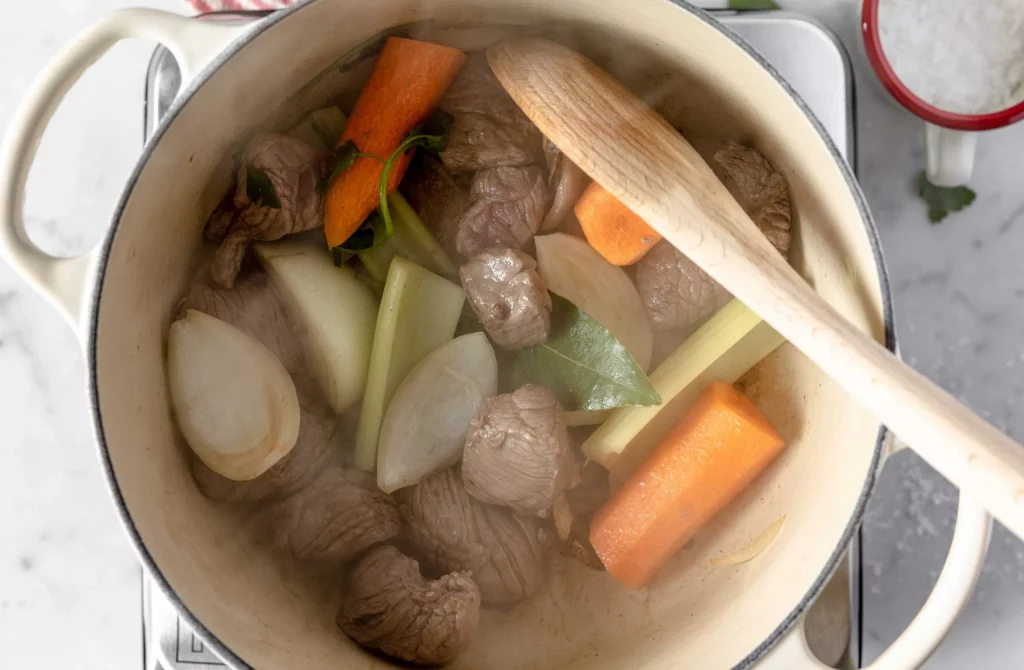 Beef stew in a pot with carrots and onions.