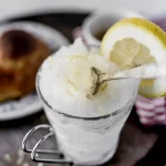 A cup of lemon ice cream with a slice of lemon.
