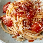 A bowl of spaghetti with tomatoes and parmesan cheese.