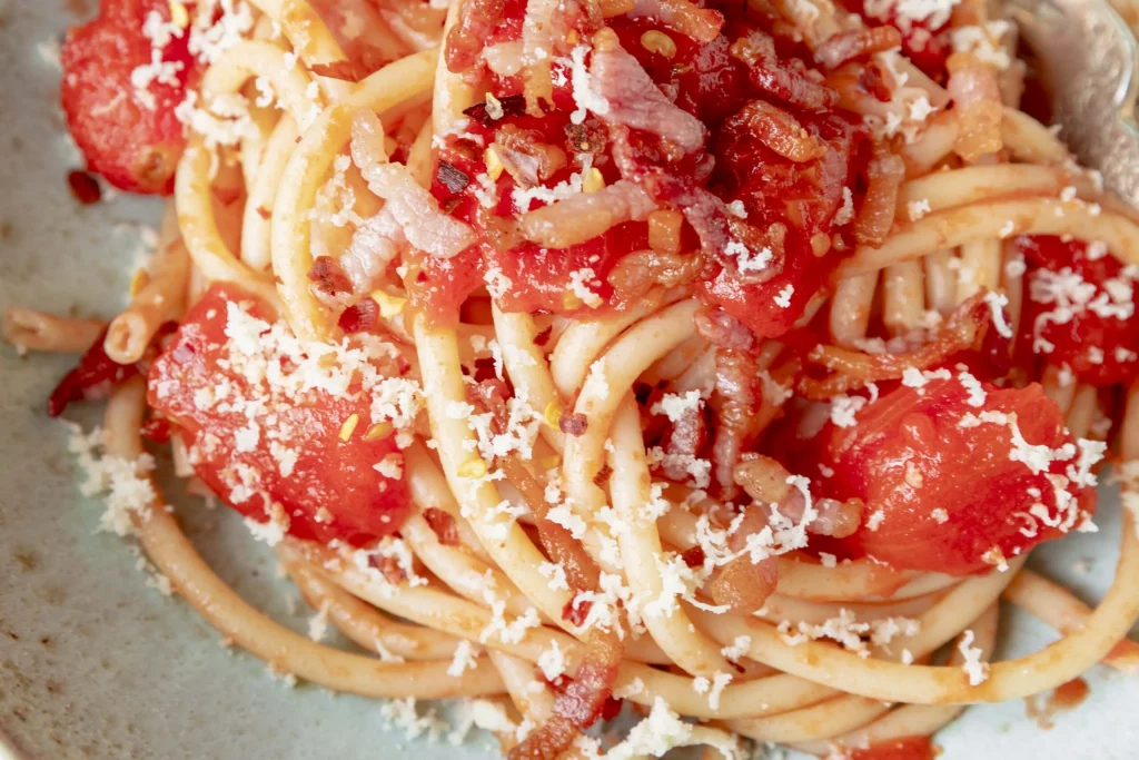A bowl of spaghetti with tomatoes, bacon and parmesan.