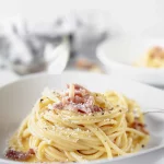 A plate of spaghetti with bacon and parmesan.