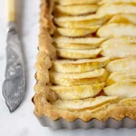 A tart with apples and a knife on top.