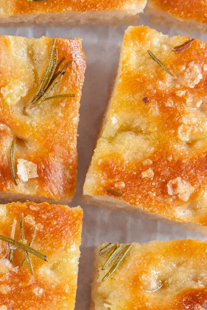 Squares of bread with sprigs of rosemary on a baking sheet.