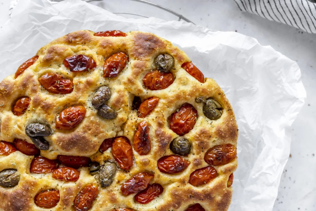 A pizza with tomatoes and olives on a plate.