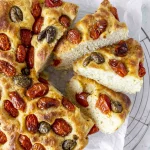 A pizza with tomatoes and olives is on a cooling rack.