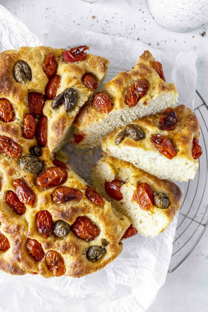A pizza with tomatoes and olives is on a cooling rack.