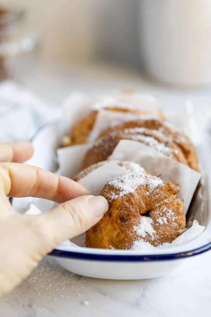 A person holding a plate of donuts with powdered sugar.