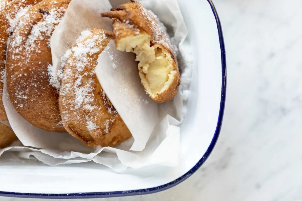 Fried doughnuts in a white bowl with powdered sugar.
