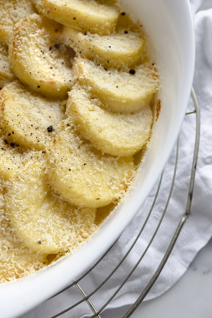 A white dish filled with sliced potatoes and parmesan.