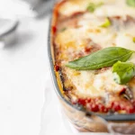 A lasagna with cheese and basil leaves on a white plate.
