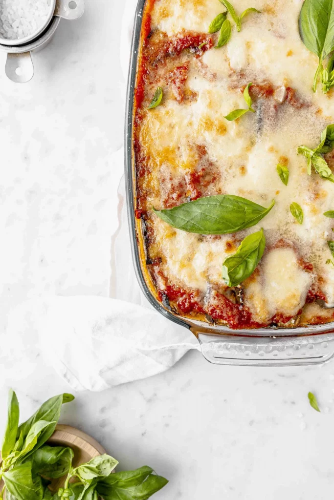 A dish of lasagna with cheese and basil leaves.