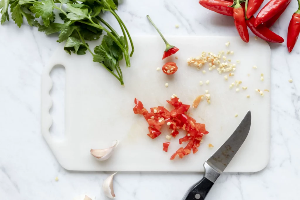 A cutting board with peppers, garlic and herbs on it.