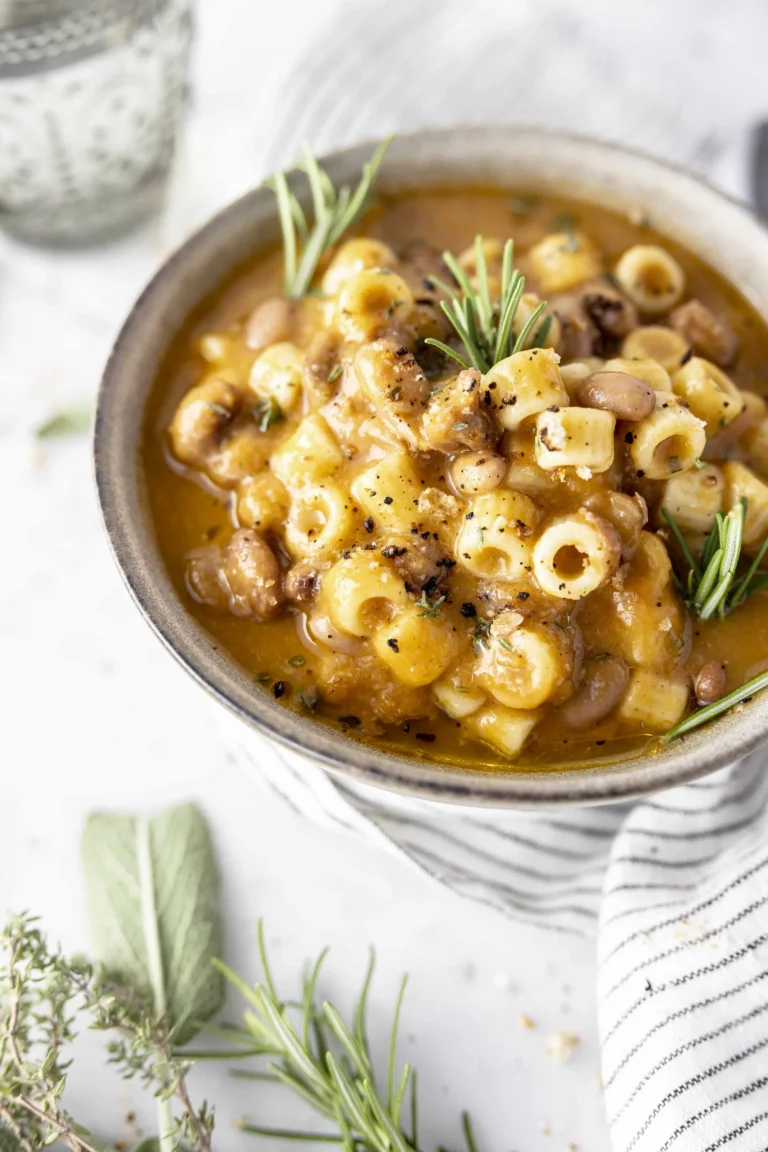 A bowl of macaroni and mushroom soup with sprigs of rosemary.