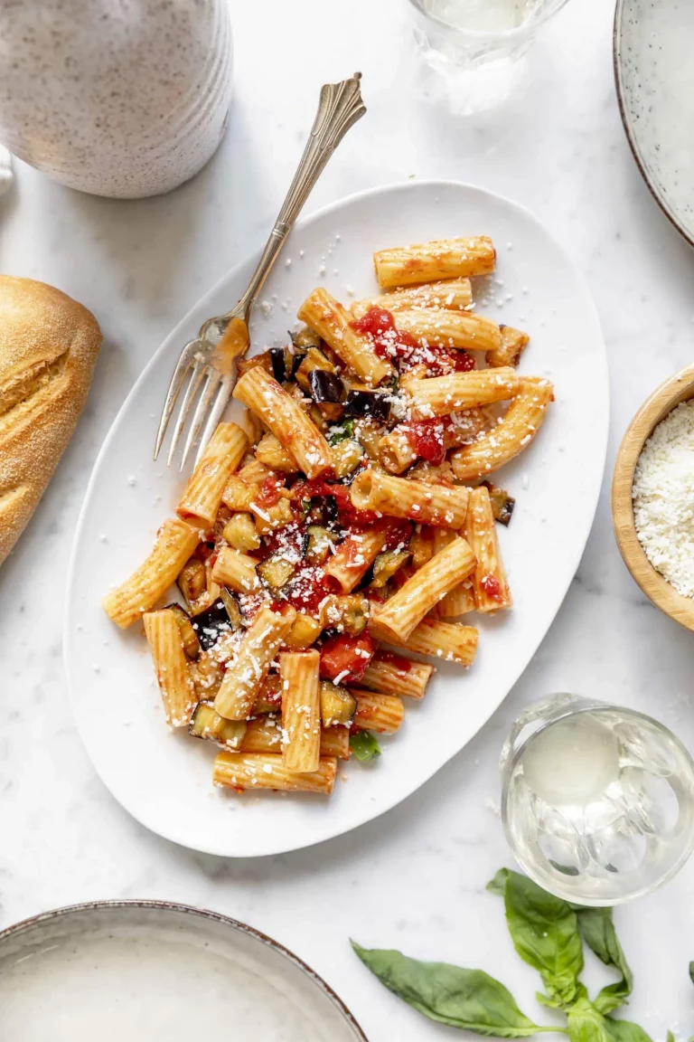 A plate of penne pasta with vegetables and bread.