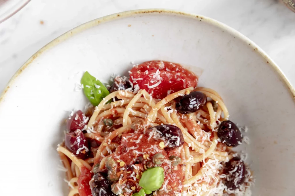 A bowl of spaghetti with tomatoes, olives and parmesan.