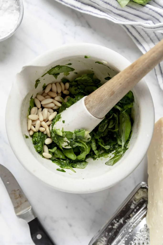 A white bowl with spinach, pine nuts and parmesan cheese.