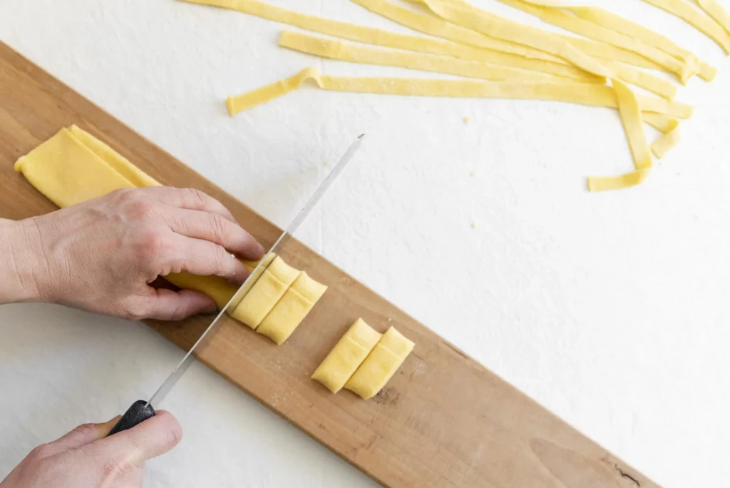 A person cutting pasta on a wooden cutting board.