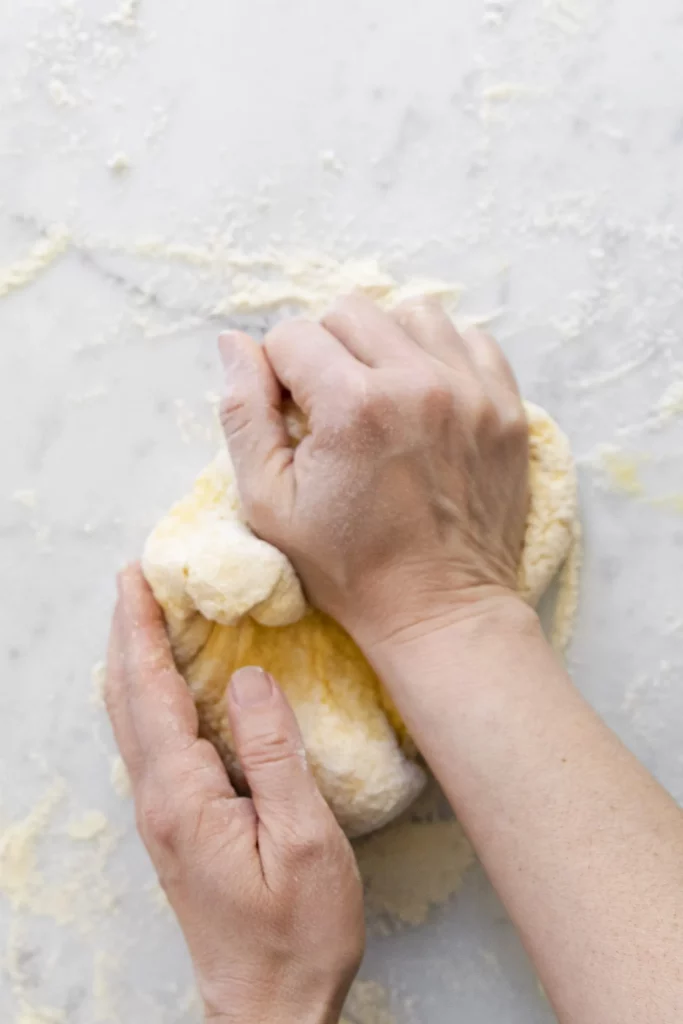 Hands kneading dough on a marble countertop.