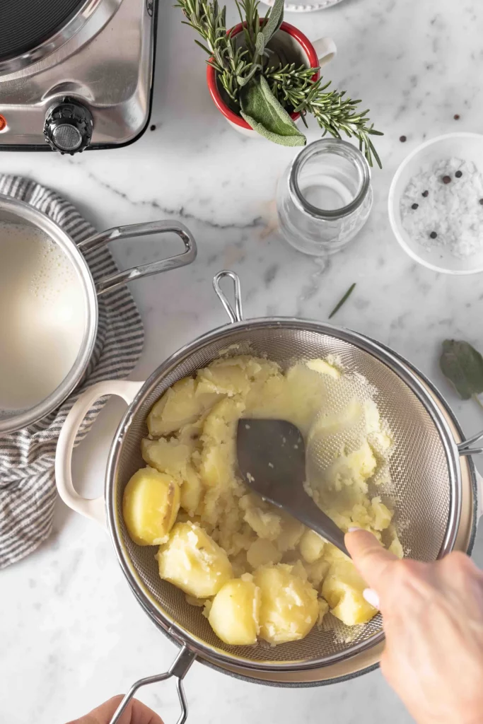 A person expertly stirs mashed potatoes in a pan on a stove.