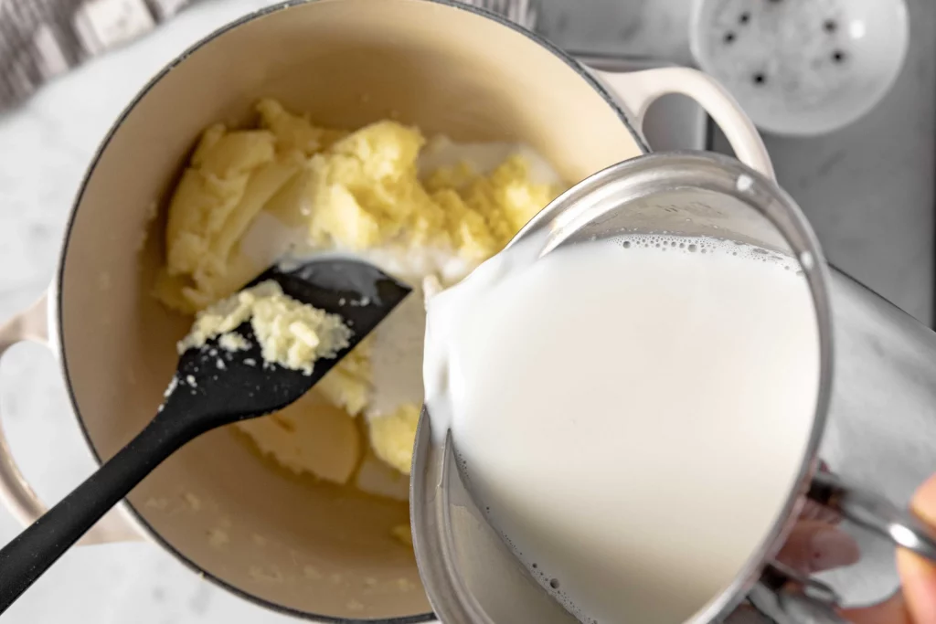 A person pouring milk into a pot to make mashed potatoes.