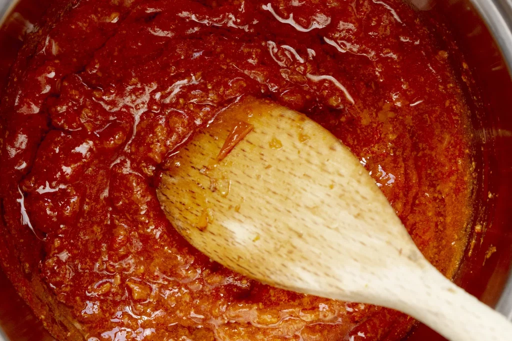 A wooden spoon in a pot of tomato sauce.