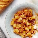 A plate of pasta with ragu neapolitan and bread next to it.