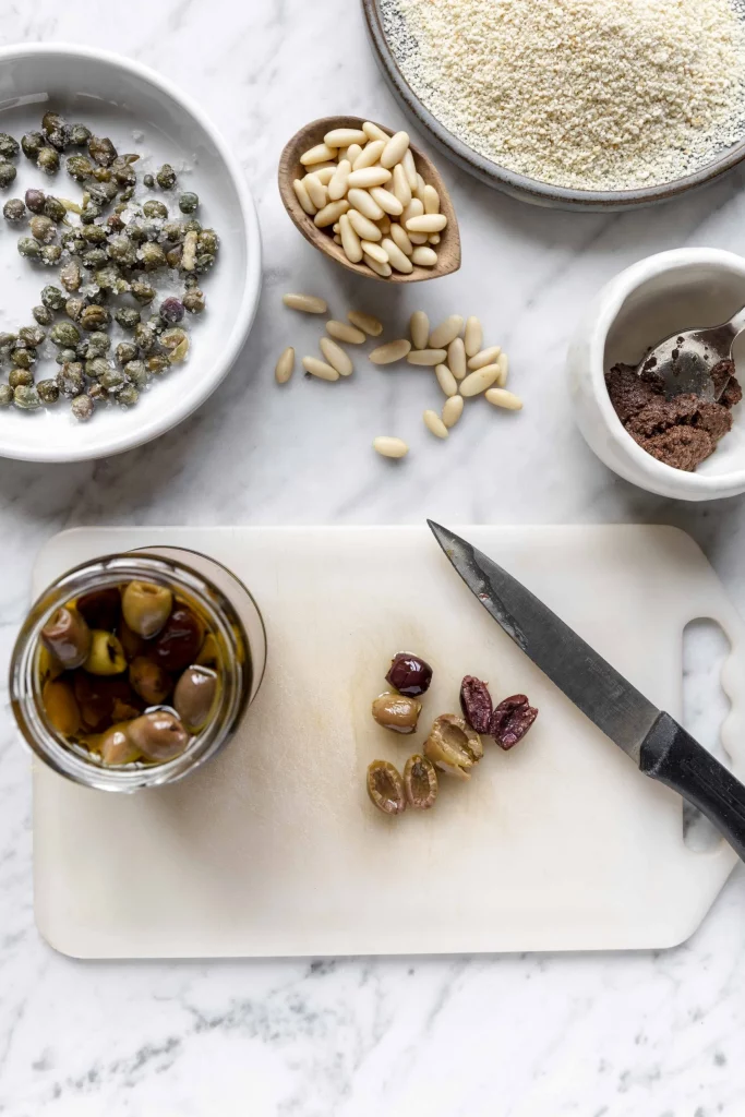 A cutting board with olives, nuts, and a knife.