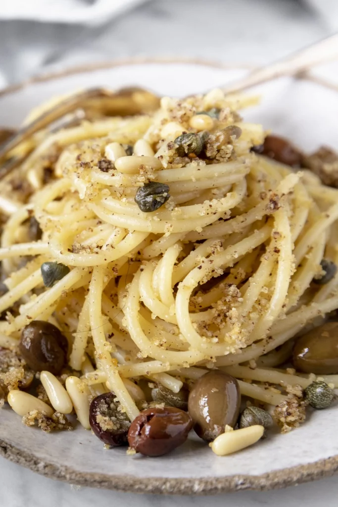 A plate of spaghetti with olives and pine nuts.