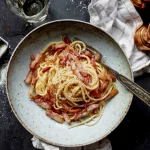 A bowl of spaghetti with bacon and parmesan cheese.