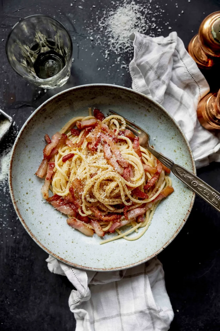 A bowl of spaghetti with bacon and parmesan cheese.