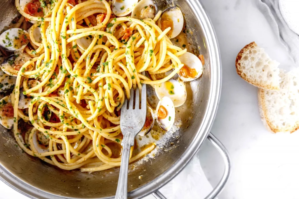 A pan full of spaghetti with clams and bread.