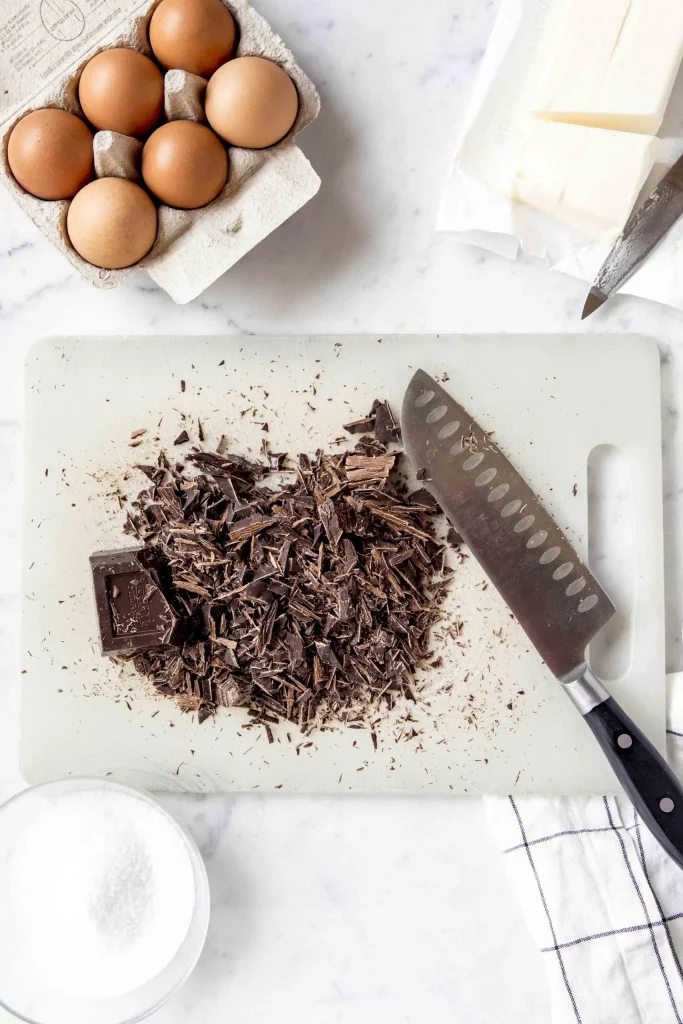 Tenerina cake topped with chocolate shavings on a cutting board next to eggs and a knife.