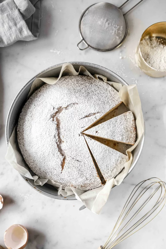 A cake in a pan with powdered sugar and utensils.