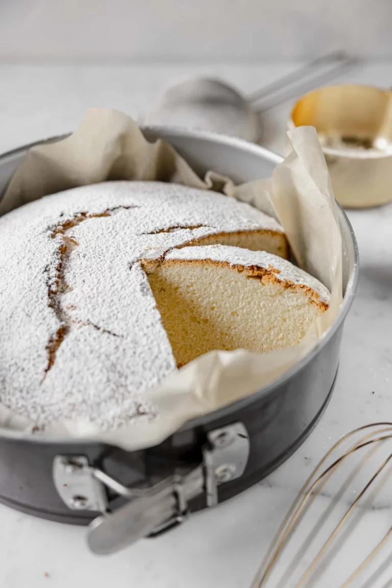 A cake in a pan with powdered sugar and a whisk.
