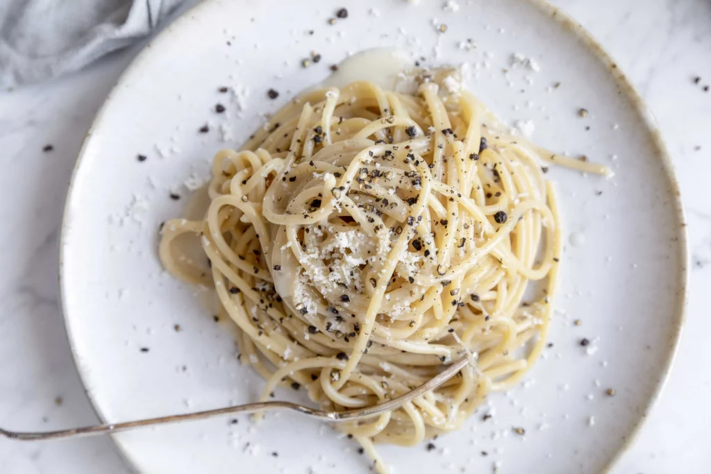 A plate of spaghetti with parmesan and black pepper.