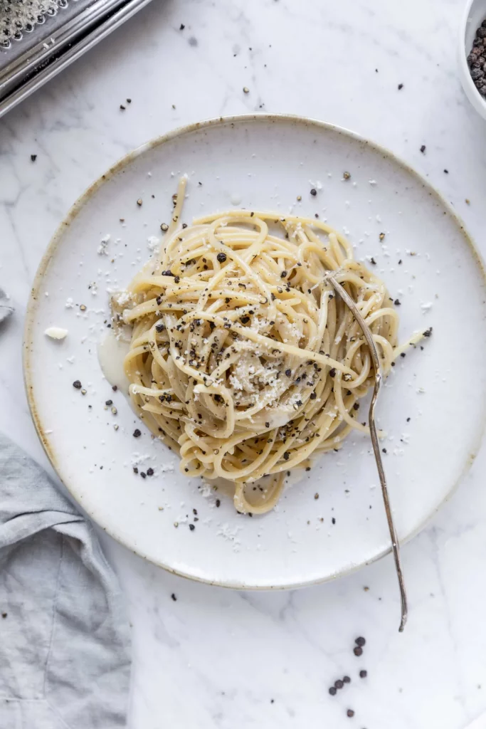 A plate of pasta with parmesan cheese and black pepper.