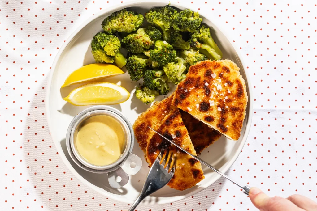 A plate with chicken, broccoli and lemon on it.
