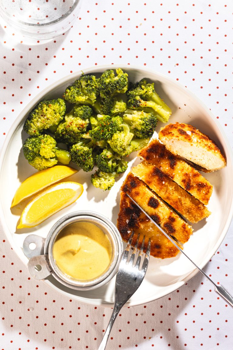A plate of breaded chicken, broccoli, and lemons.